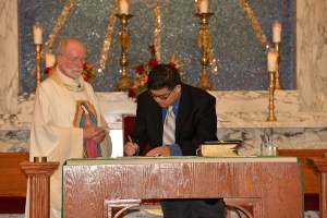 Joseph signs his vow renewal while Fr. Ed Kilianski, pastor of OLG, looks on.